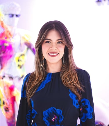 Natalia Devia sonriendo, con vestido azul de flores, frente a arte colorido