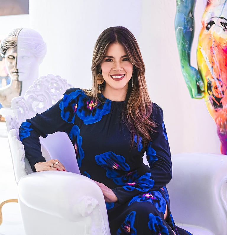 Natalia Devia sentada en un sillón blanco, rodeada de esculturas y arte colorido
